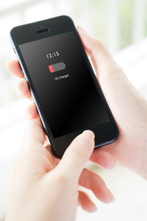 Female hand holding mobile phone with low charged battery screenの写真素材