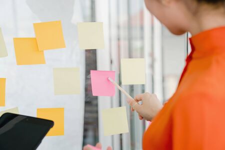 Businesswoman writing on colorful sticky note paper in business office, close up of hand
