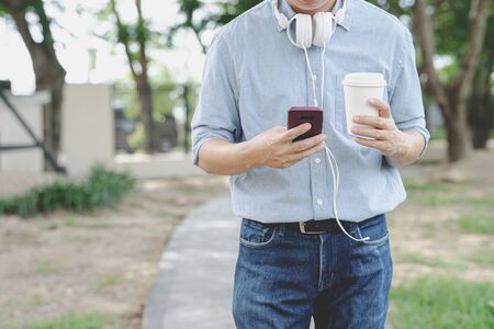 Businessman use smartphone and hold cup coffee in park alone