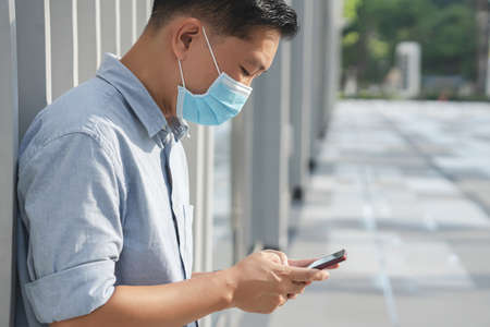 Businessman on the street with a blue face mask staring at his cell phoneの写真素材
