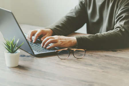 Man typing on a laptop keyboard on a wooden table and tree. Business conceptの写真素材