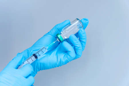 isolated on blue background: doctor's hand in glove holds a syringe vaccination against virus...