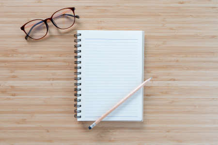 notepad, glasses and pencil on light wood table background. Copy space for your text. Flat lay.