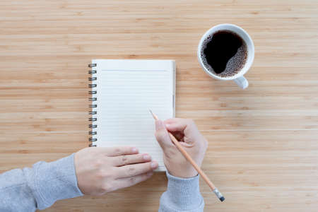 notebook with hand hold pencil and coffee on old wooden table.Top view. Flat lay.の写真素材