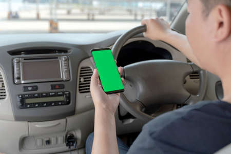 Mock up of man using mobile smart phone inside a car. Driver hand holding blank green screen...