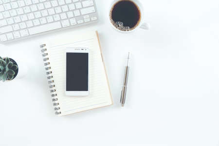 Modern white office desk table with laptop computer, smartphone with black screen over a notebook...