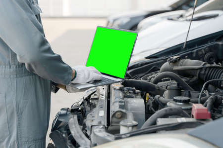 Skilled mechanic using a laptop computer green screen to check collect information during work a car engine. service maintenance of industrial to engine repair.の写真素材