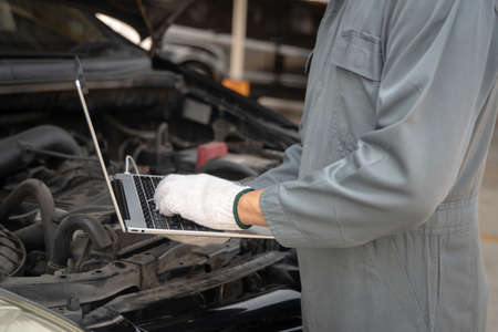 Skilled mechanic using a laptop computer to check collect information during work a car engine....