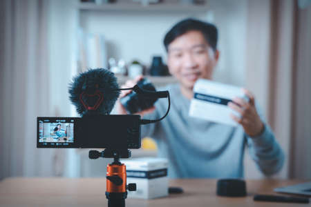 Close up of camera screen. Young male technology blogger recording video blog or vlog review of new camera lens at home studio. Blogging, Work from Home concept. Focus on camera screenの写真素材