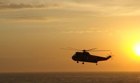 helicopter flying over ocean at sunsetの写真素材
