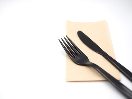 Black plastic fork and knife place on a recycle napkin paper and focus around top area on the fork and knife and blur out other area of the picture with white backgroundの写真素材