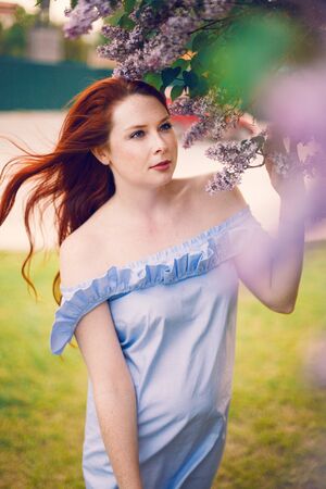 Model Olesya is posing in a dress by a blooming lilac in the summer.