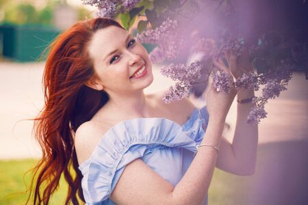 Model Olesya is posing in a dress by a blooming lilac in the summer.