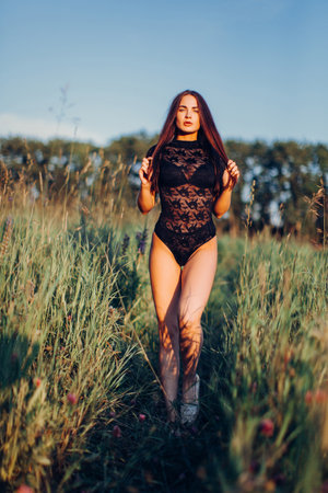 Brunette in lace black bodysuit posing in the field at sunsetの写真素材