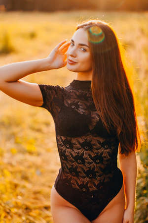 Brunette in lace black bodysuit posing in the field at sunsetの写真素材