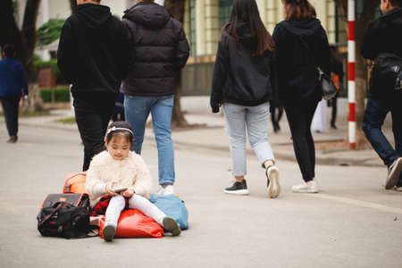 Vietnam. Hanoi. January 13, 2018. A little girl is sitting on things and waiting for her parents on the streetのeditorial素材
