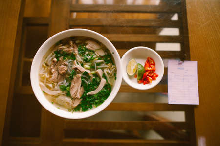 A bowl of famous Vietnamese pho noodle soup with rare beef, tendons, tripe and brisket, served with herbs. Intentional shallow depth of field against the background.の写真素材