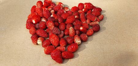 Delicious wild strawberries in the shape of heart isolated on a light brown backgroundの写真素材