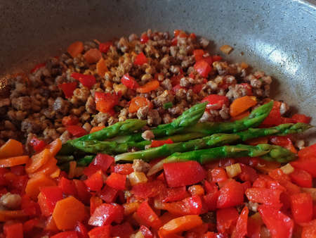 Top view of green asparagus, red vegetables and minced meat in a pan food backgroundの写真素材