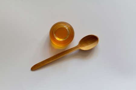 Honey in a glass jar and a wooden spoon isolated on a white background, food and drink conceptの写真素材