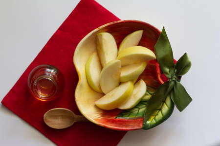 Apples cut into slices in an apple-shaped plate on a red linen napkin a white background, jar with honey copy spaceの写真素材