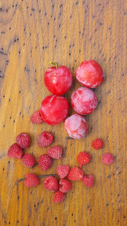 Red plums and raspberries on a wooden brown natural rustic backgroundの写真素材