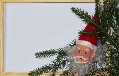 Christmas or winter composition. Santa's head with a red hat, white background, wooden rustic frame, with spruce branch decoration. Christmas background, Christmas, winter, new year concept. Flat lay, top view, copy space, 2021の写真素材