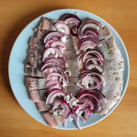 Herring fillet with spices and red onions served on a plate. Wooden rustic background, top view. Cold appetizer. Food backgroudの写真素材