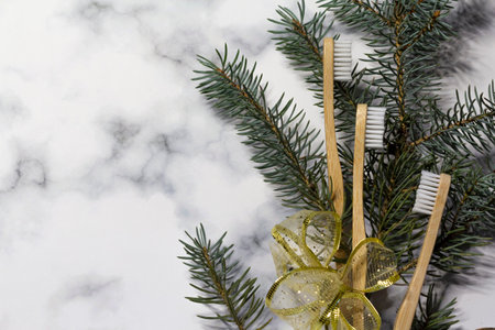 On a white-gray marble background, three bamboo toothbrushes, a spruce branch and a yellow ribbon. Zero waste concept, no plastic and safe the planet conceptの写真素材