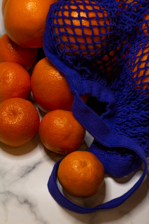 Oranges in a reusable mesh shopping basket on a white-gray marble background. Zero waste concept, no plastic and safe the planet conceptの写真素材