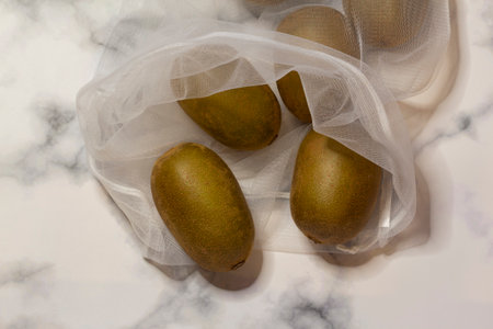 Reusable white mesh shopping bag with fruit, kiwi White-gray marble background. Zero waste concept, no plastic and safe the planet conceptの写真素材