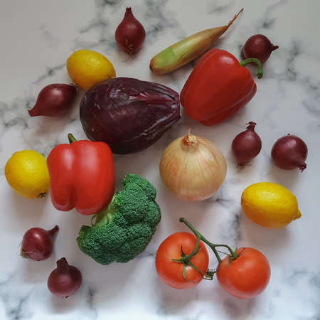 Various vegetables red and yellow onions, broccoli, tomatoes, peppers, lemons on a white-gray marble background. Vitamins, healthy choices, immune system strengthening, antioxidants, food, organic farming, agricultureの写真素材