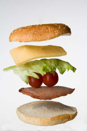 Sandwich made of white buns, meat, tomatoes, cheese, salad arranged horizontally and isolated on a white background. Creative food presentationの写真素材