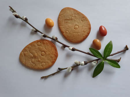 Easter background. Egg shaped cookies, spring tree branches, colored round candies on a white...