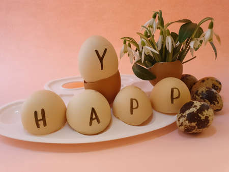 the inscription happy on the egg shell and Quail Easter eggs and spring flowers on a peach color background. Easter greeting, postcard, copy space, easter decorations rusticの写真素材