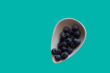 Blueberry berries in a white plate on a turquoise background. Food background, copy space, healthy foodの写真素材