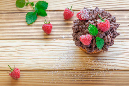 Cupcake, muffin with chocolate cream decorated with raspberries and mint. Light wooden background.の写真素材
