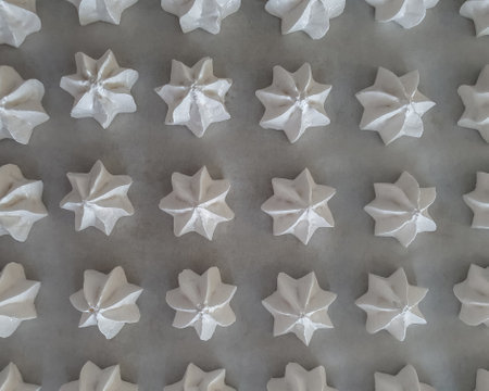 Pattern with delicate white meringue cookies. Meringues are lying in rows on a baking paper as a background. Directly above, horizontalの写真素材