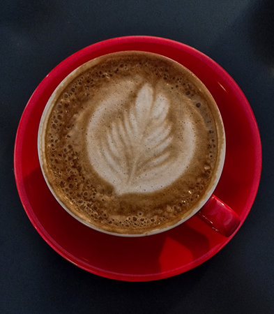 red cup of coffee, latte art in heart shape, dark grey background, milk foamの写真素材