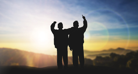 silhouette mans with hands raised on blurred city with sunset backgroundの写真素材