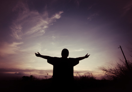 silhouette man with hands raised on blurred city with sunset backgroundの写真素材