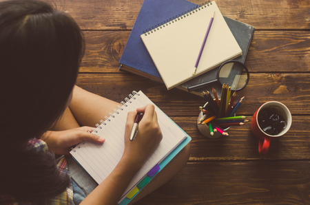 Girls are pen to write on the notebook on wood floorの写真素材