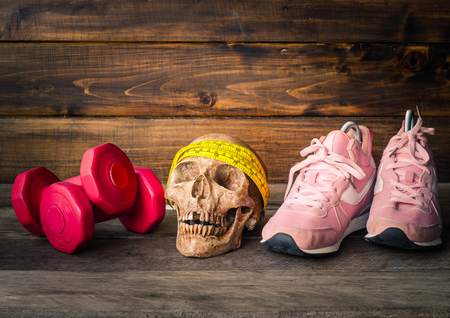 The skull and fitness concept with exercise equipment on wooden background.の写真素材