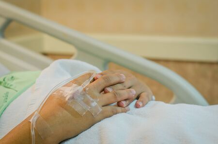 Hand of Male patient lying on a hospital bed receiving saline.の写真素材