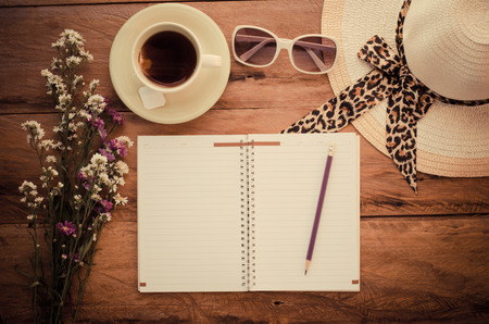 Pencil on notebook Include sunglasses, tea cup, hat and flower on the wooden background.