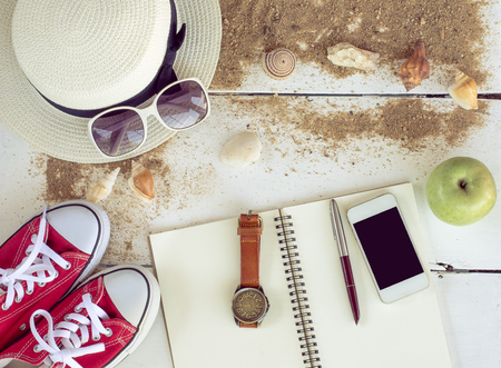 Travel accessories, hats, sunglasses, notebook, pen, phone, shell, placed on a wooden floorの写真素材