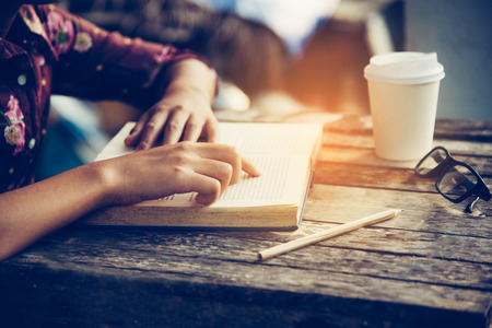 Focus hand open book for reading on wooden table with gold lighting at the morning の写真素材