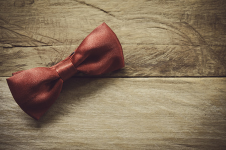 Red bow tie placed on wooden floor.