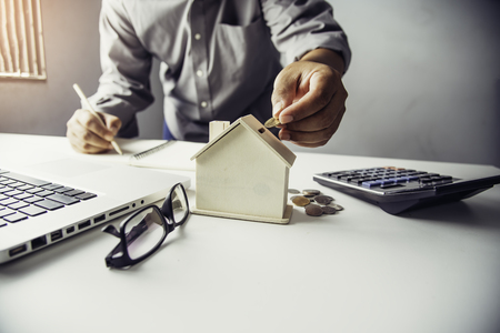 Hand business putting money coin  with wooden house,Property investment and house mortgage financial conceptの写真素材