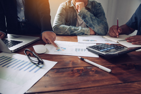 Business team working with laptop and calculator in open space office. Meeting report in progressの写真素材